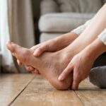 A close-up view of a person gently massaging the base of their foot and toes
