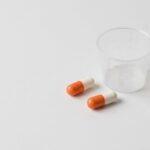 A clear, overhead shot of two generic orange and white ibuprofen pills resting next to a small dosage measuring cup on